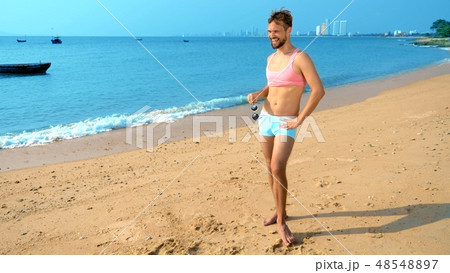 Playful handsome guy in a pink t-shirt and blue shorts rejoices at the beach. freak on the sea. Playful handsome guy in a pink t-shirt and blue shorts rejoices at the beach. freak on the sea. 48548897