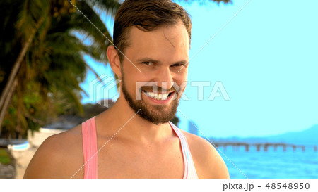 Close-up, Playful handsome guy in pink t-shirt on a tropical beach. he looks at the camera, rejoices 48548950