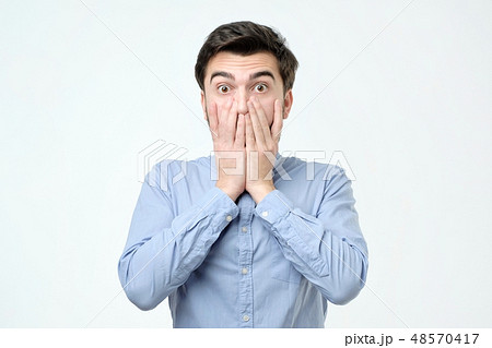 Young hispanic man covering his mouth with hand Young hispanic man covering his mouth with hand 48570417
