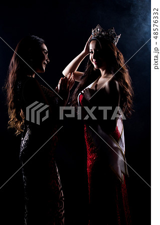 Portrait of Two Miss Asian Women Pageant Beauty Contest in Evening Ball Gown dress, look waiting final announcement moment, studio lighting dark smoke background low key exposure silhouette copy spac 48576332
