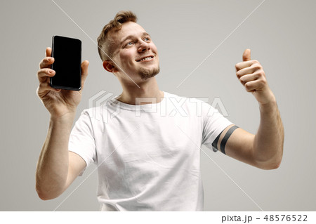 Young handsome man showing smartphone screen isolated on gray background in shock with a surprise 48576522