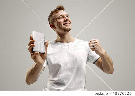 Young handsome man showing smartphone screen isolated on gray background in shock with a surprise 48576529