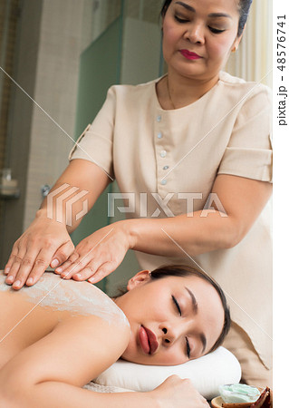 Professional Therapist scrub with light gentle green herbal Beauty Treatment on Mix Race Caucasian Asian woman skin back in the Health Spa, for smooth clean refresh new skin by scrubing old one 48576741