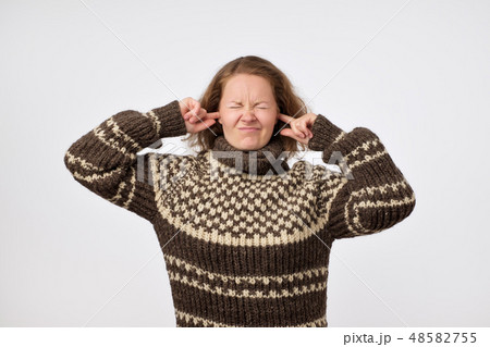 female in warm brown sweater plugging her ears  48582755