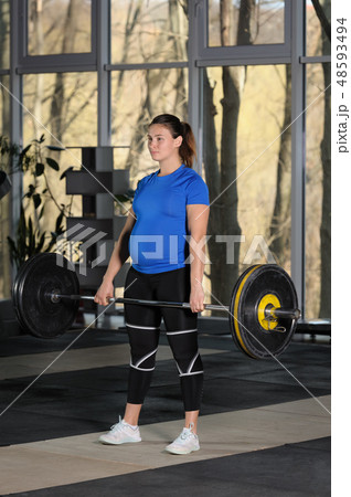 Young woman doing deadlift workout with heavy barbell in dark gym 48593494