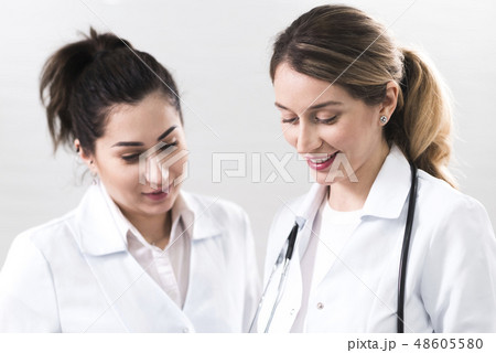 Two female assistants dressed in white coats talking to each other in the dentistry center 48605580