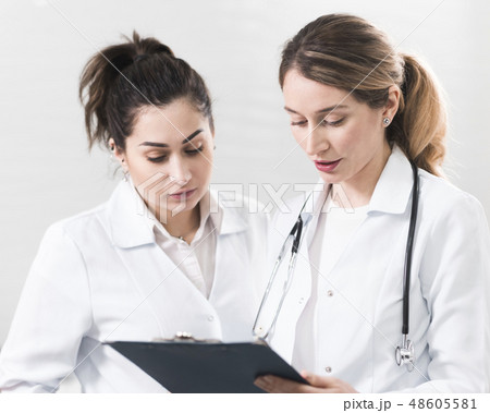 Two female assistants dressed in white coats talking to each other in the dentistry center 48605581