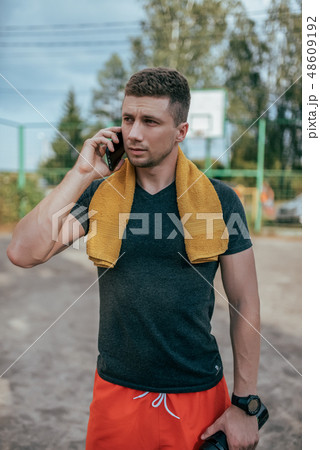 A male athlete holds a phone in his hand, calls on the phone, and rests after a workout in the fresh A male athlete holds a phone in his hand, calls on the phone, and rests after a workout in the fresh 48609192