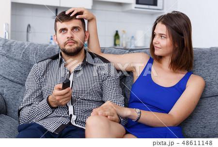 Young man and woman sitting on sofa at home watching TV Young man and woman sitting on sofa at home watching TV 48611148