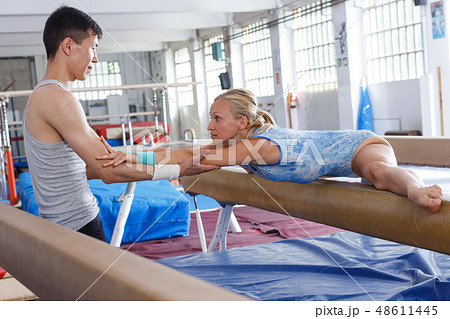 Woman in bodysuit training at broad bars in sport gym, man helping Woman in bodysuit training at broad bars in sport gym, man helping 48611445