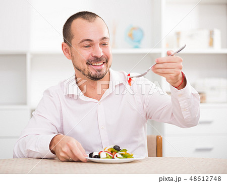 Positive young man eating greek salad Positive young man eating greek salad 48612748