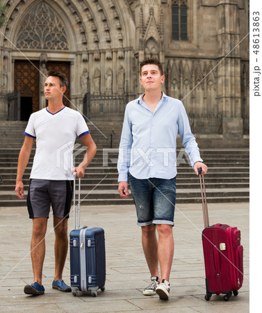Men in shorts with luggage walking through city street Men in shorts with luggage walking through city street 48613863