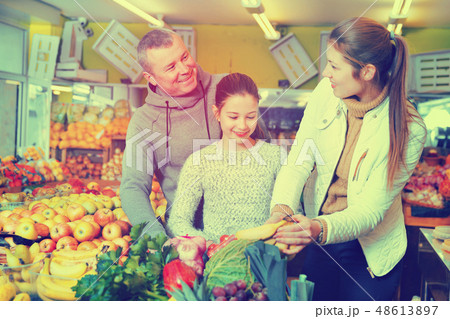 Parents with daughter choosing sweet bananas in fruit market 48613897