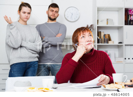 Distressed aged woman with paperwork and irritated family behind Distressed aged woman with paperwork and irritated family behind 48614005