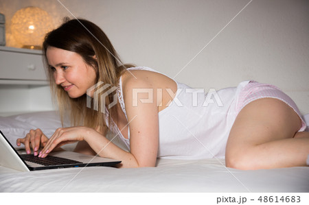 Attractive girl is lying with laptop on bed in bedroom in home 48614683