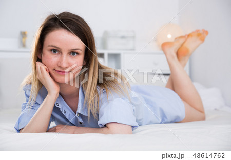 Attractive girl in blue shirt lying in bed in home interior 48614762