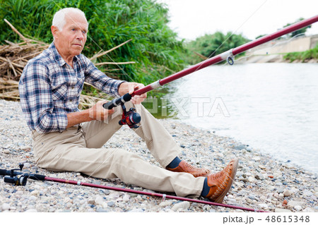 Aged man fishing at lakeside Aged man fishing at lakeside 48615348