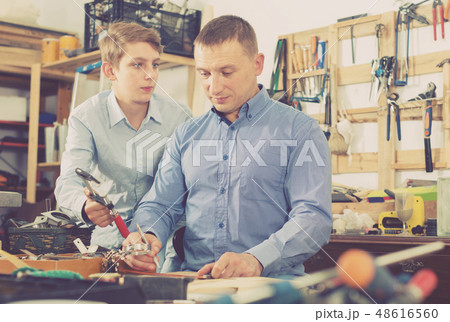father and teen son working with wood plank in workshop father and teen son working with wood plank in workshop 48616560