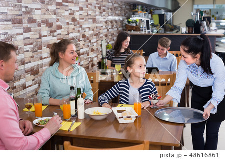 Young smiling girl is bringing delicious dessert to young visitors Young smiling girl is bringing delicious dessert to young visitors 48616861