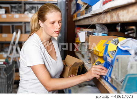 Young woman choosing construction materials at shelves in modern building shop Young woman choosing construction materials at shelves in modern building shop 48617073