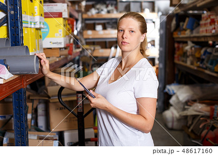 Young woman standing near racks in build store bebore buying tools Young woman standing near racks in build store bebore buying tools 48617160