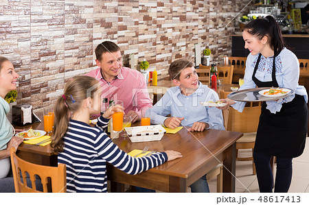 Polite cheerful waitress bringing ordered dishes to family 48617413