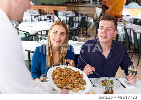 Waiter serving tasty dishes to couple Waiter serving tasty dishes to couple 48617723