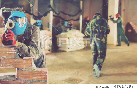 Portrait of blue team player who is aiming in opponents on paintball field. 48617995