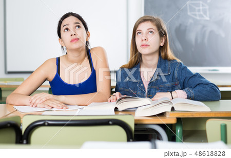 Young girls are sitting at the desk and reading text in the classroom 48618828