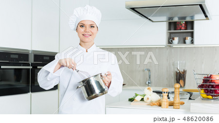 Cheerful woman chef preparing food with whisk on kitchen 48620086