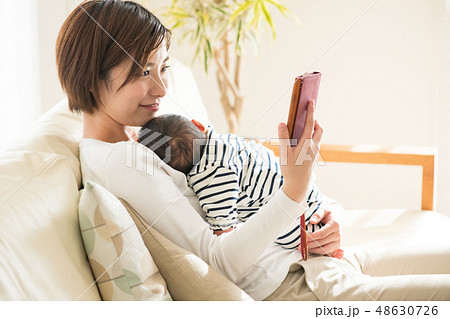 眠る赤ちゃんを抱きながらスマホを見る母親 育児 子育て 48630726