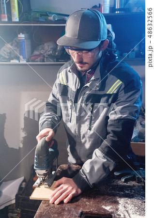 Young man with a beard in gray overalls and goggles by profession a carpenter works as an electric 48632566
