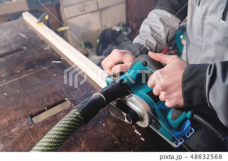 Close-up of a carpenter's hand working with an electric plane with suction of sawdust. Leveling and 48632568