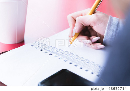 Close-up from behind the back of a young woman in a winter polto is holding a ballpoint pen and is 48632714