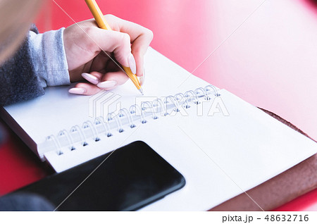 Close-up from behind the back of a young woman in a winter polto is holding a ballpoint pen and is 48632716