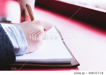 Close-up from behind the back of a young woman in a winter polto is holding a ballpoint pen and is 48632718