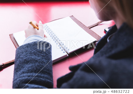 Close-up from behind the back of a young woman in a winter polto is holding a ballpoint pen and is 48632722