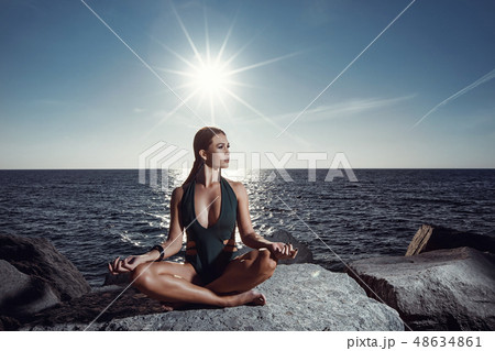 Beautiful girl in a swimsuit doing yoga on a rock 48634861