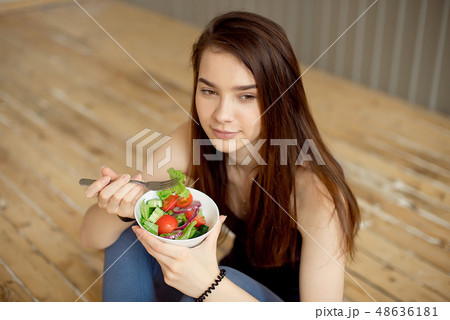 Sports beautiful girl sitting on the floor and eating a salad from fresh vegetables and greens 48636181