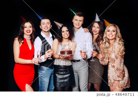 Pretty girl with birthday cake and her friends looking at burning candles at party 48640711