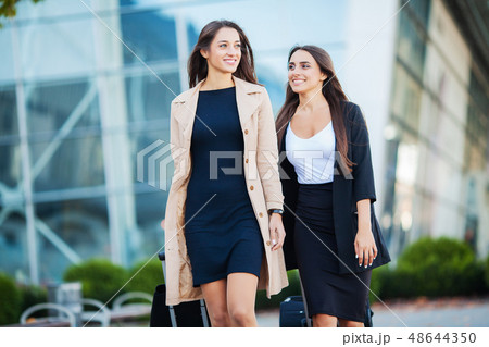 Vacation. Two happy girls traveling abroad together, carrying suitcase luggage in airport Vacation. Two happy girls traveling abroad together, carrying suitcase luggage in airport 48644350
