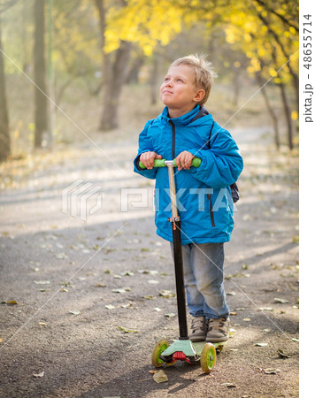A boy riding a scooter in the autumn park. A boy riding a scooter in the autumn park. 48655714