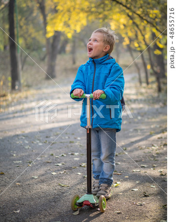 A boy riding a scooter in the autumn park. A boy riding a scooter in the autumn park. 48655716