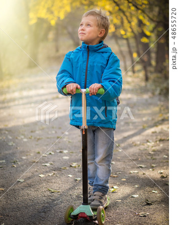 A boy riding a scooter in the autumn park. A boy riding a scooter in the autumn park. 48655720