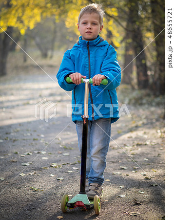 A boy riding a scooter in the autumn park. A boy riding a scooter in the autumn park. 48655721