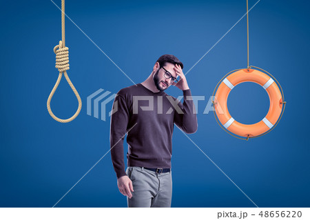 Man in casual outfit standing half-turn with hand on forehead as if choosing between lifebuoy 48656220
