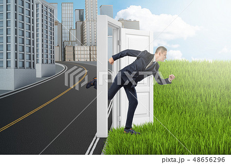 Side view of businessman running from modern city to green field through door standing alone between Side view of businessman running from modern city to green field through door standing alone between 48656296