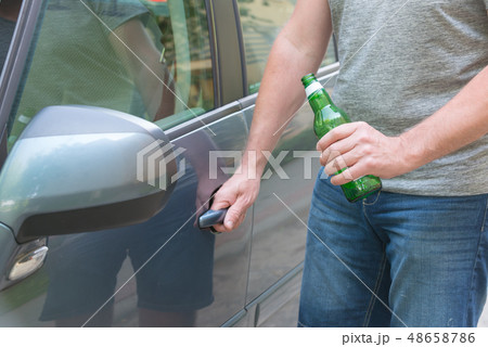 Man opening his car while holding a bottle of beer Man opening his car while holding a bottle of beer 48658786