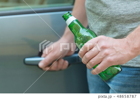 Man opening his car while holding a bottle of beer 48658787