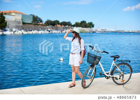 Happy attractive girl in sunglasses and with backpack riding a bike along stony sidewalk Happy attractive girl in sunglasses and with backpack riding a bike along stony sidewalk 48665873